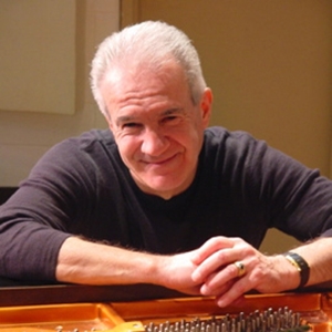 Colour photograph of American composer Denis Leogrande. sitting at a piano with his hands crossed.