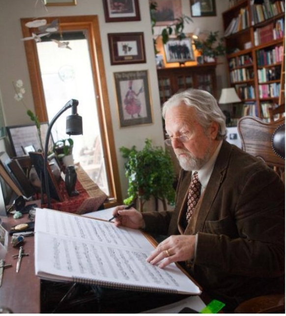 Photograph of composer Eric Funk sitting at hi desk with his hand on a music manuscript.