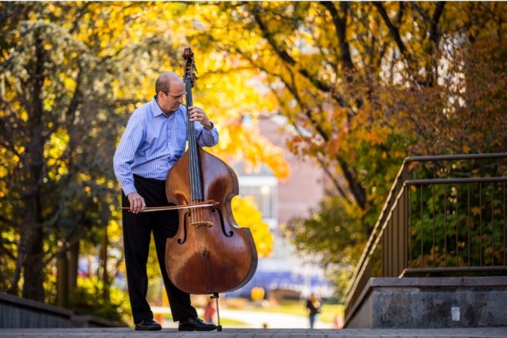 Image of double bass composer Eric Hansen stood with his bass in an autumnal park