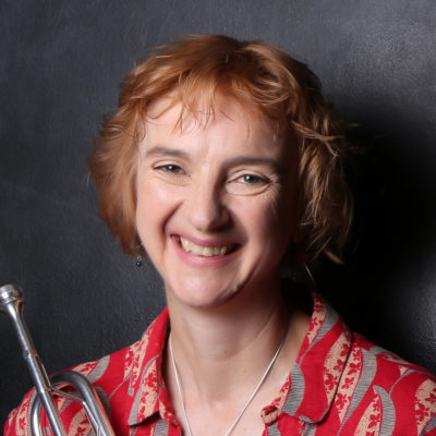 Photograph Image of female composer Kay Charlton wearing a patterend red shirt and holding a silver trumpet