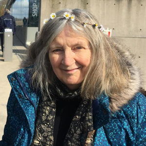 Image of musician Lucy Akehurst with diasies in her hair and wearing a blue coat