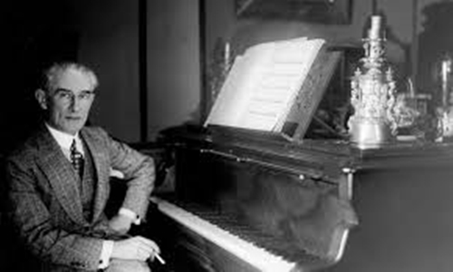 Photograph of French composer Maurice Ravel sitting at a piano and smoking a cigarette.