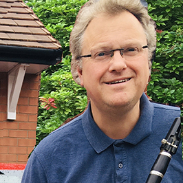 Photograph of British composer Andrew Wilson. He is wearing a blue shirt and is holding a clarinet.