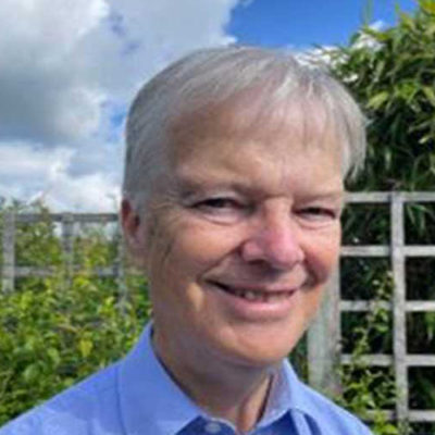 Colour photograph of Yorkshire composer Stephen Binnington in a garden on a sunny day, and wearing a blue shirt.